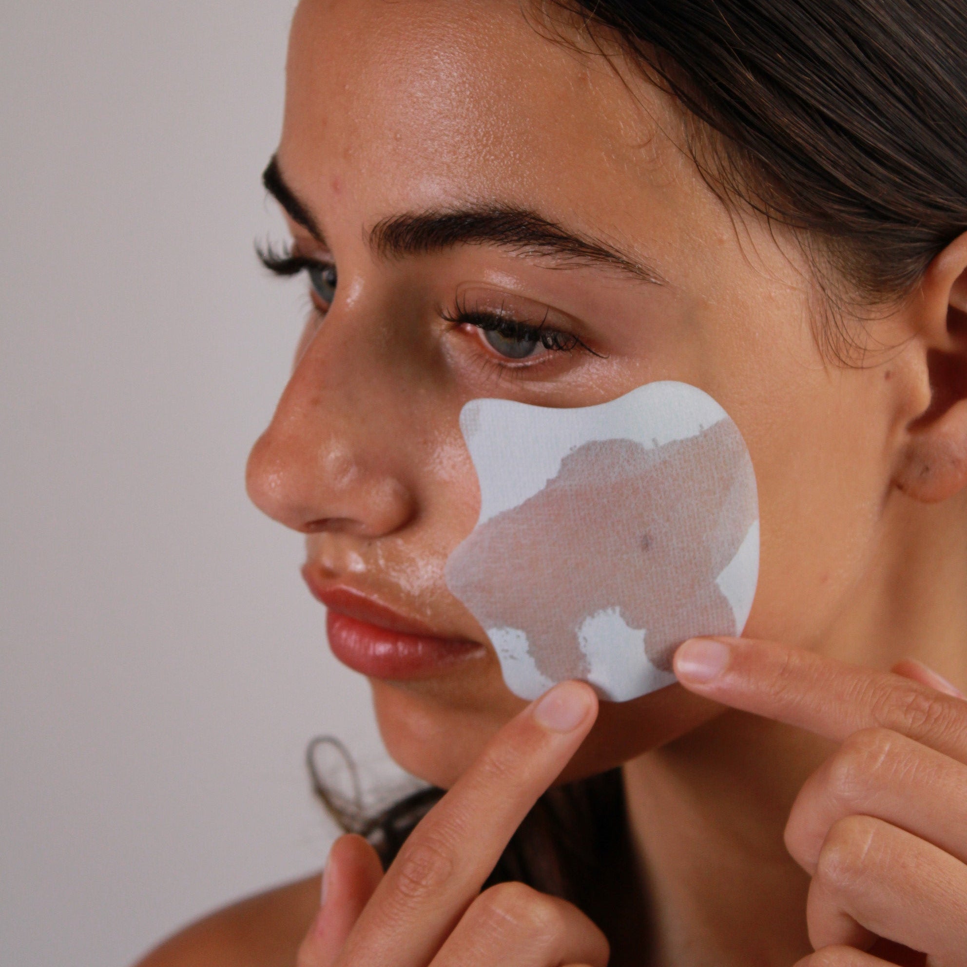 Person applying a patch for natural products for acne treatment on their face for calming benefits.