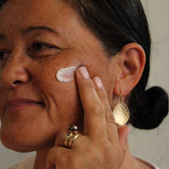 Woman applying cream to her cheek, demonstrating how to care for tight skin.
