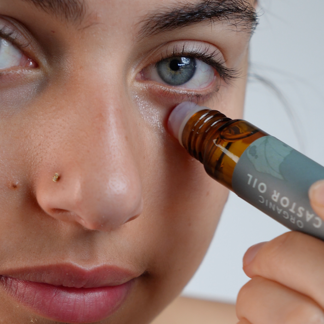 Woman applying castor oil under her eyes showcasing the castor oil skin benefits.