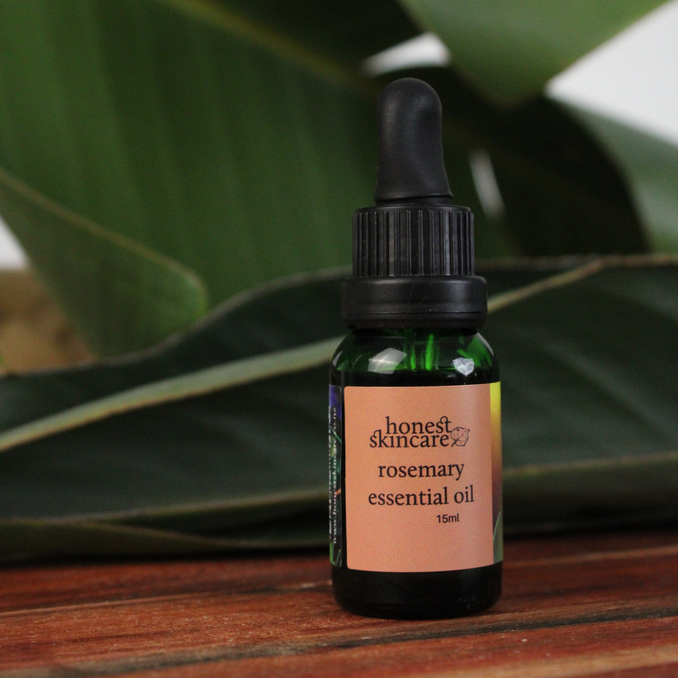 Brown glass bottle with a dropper being filled with Rosemary essential oil 15ml honest skincare against a green leafy background