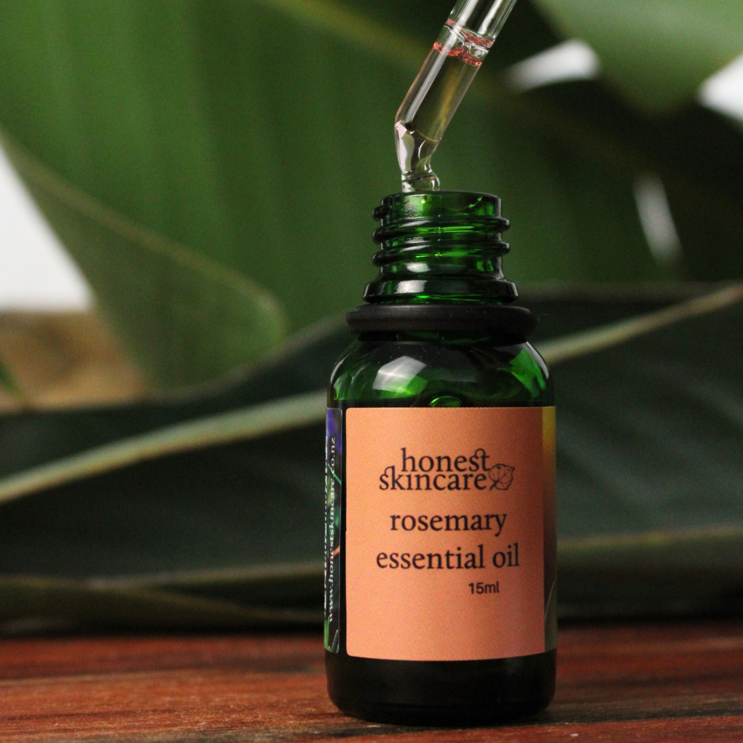 Green bottle of Rosemary essential oil 15ml honest skincare with a dropper against a green leafy background