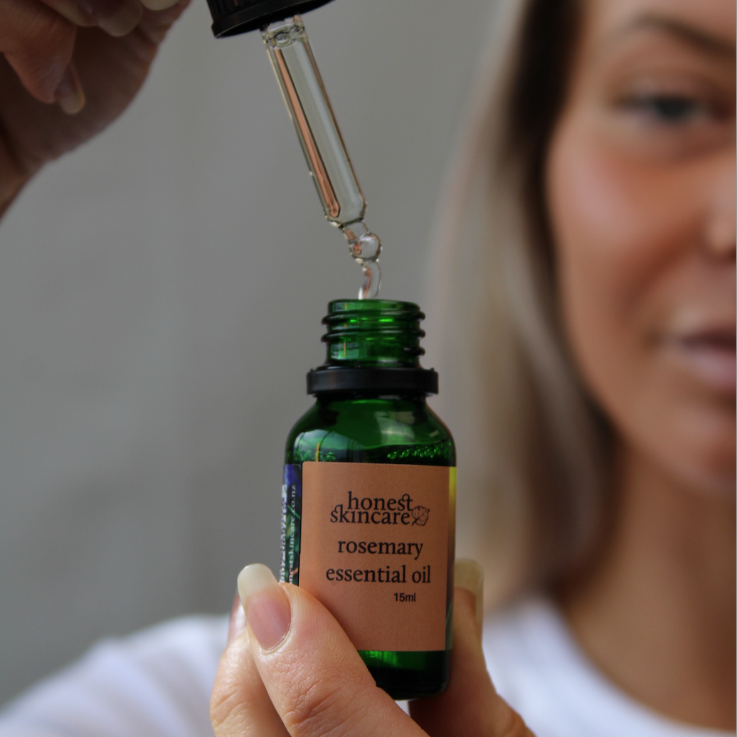 Person holding a bottle of ' honest skincare' rosemary essential oil with a dropper.