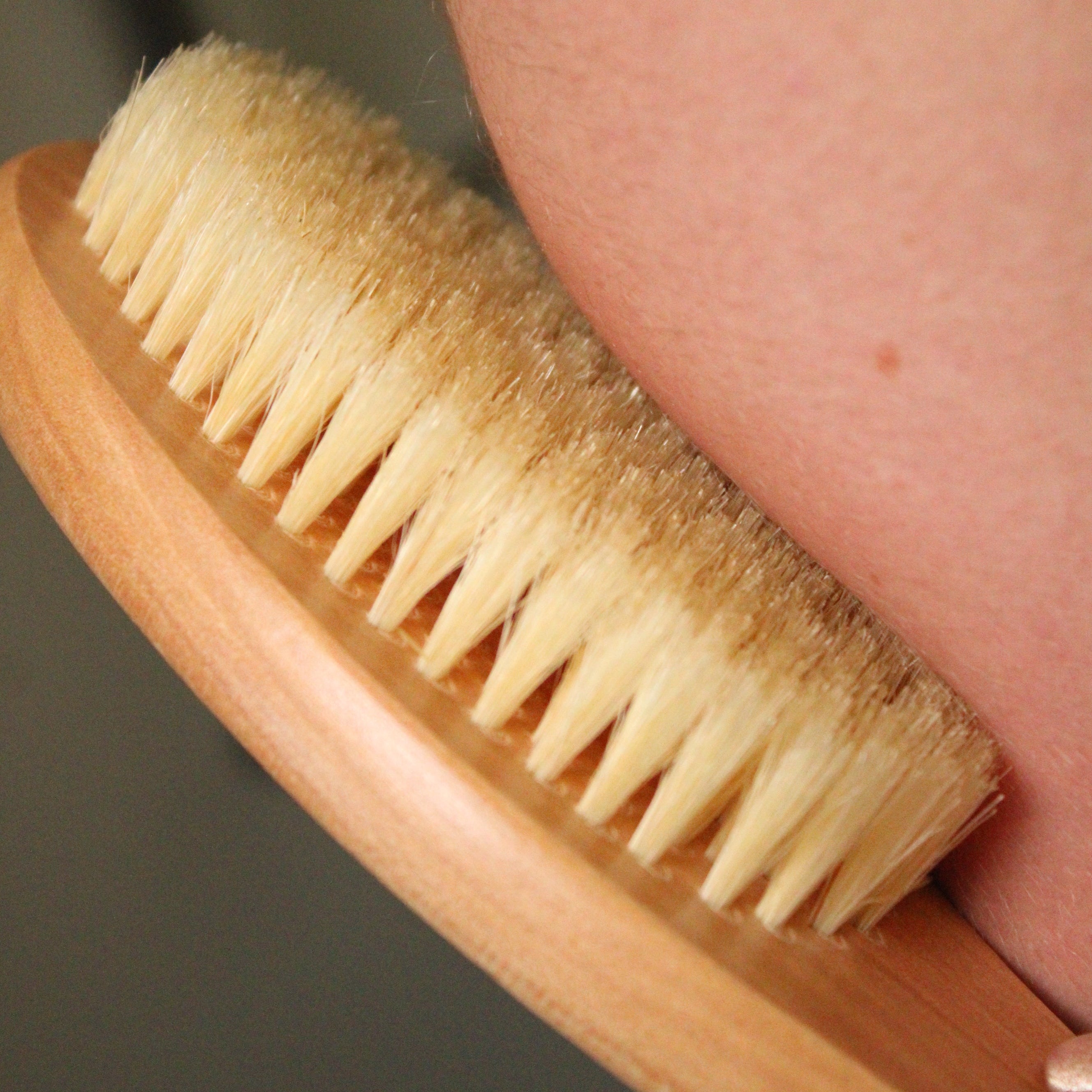 Wooden brush with natural bristles being used on a person's skin.