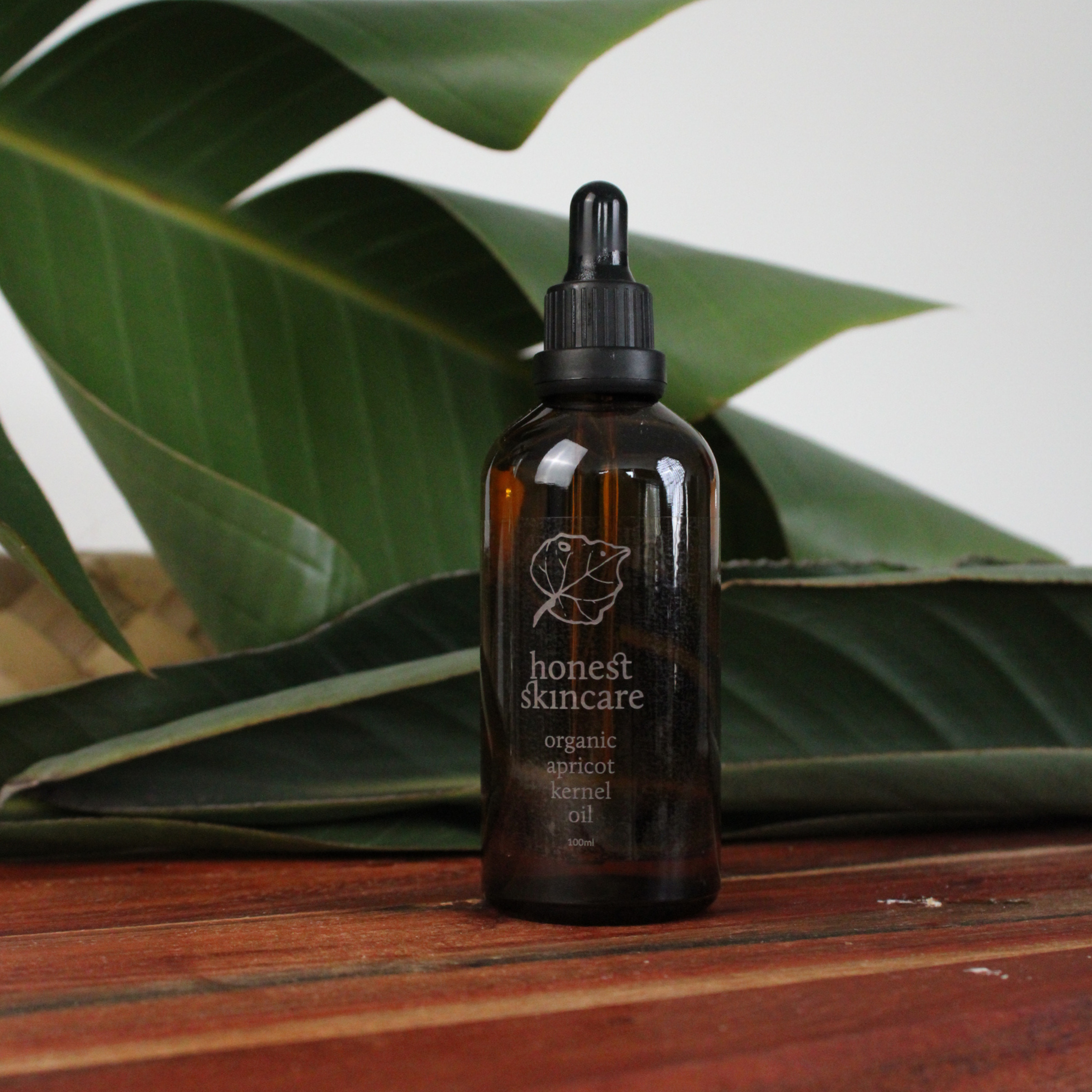 Brown glass bottle with dropper apricot kernel oil 100ml amber glass on a wooden surface with green leaves in the background