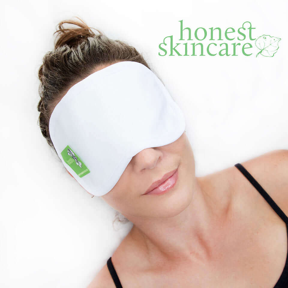 Woman wearing a white organic cotton eye mask with 'honest skincare' branding on a white background