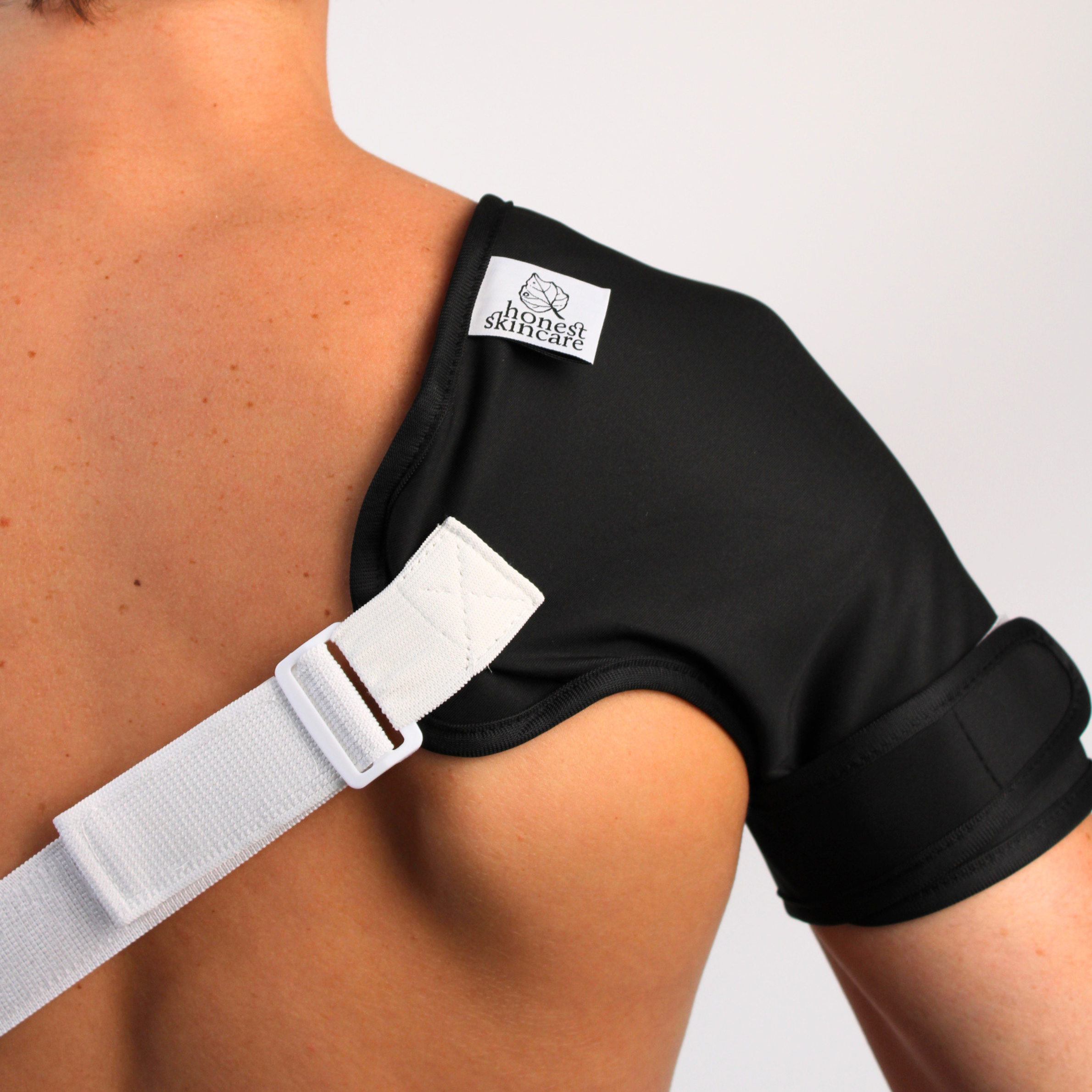 castor oil shoulder wrap with a white strap on a person's shoulder, featuring a honest skincare label.