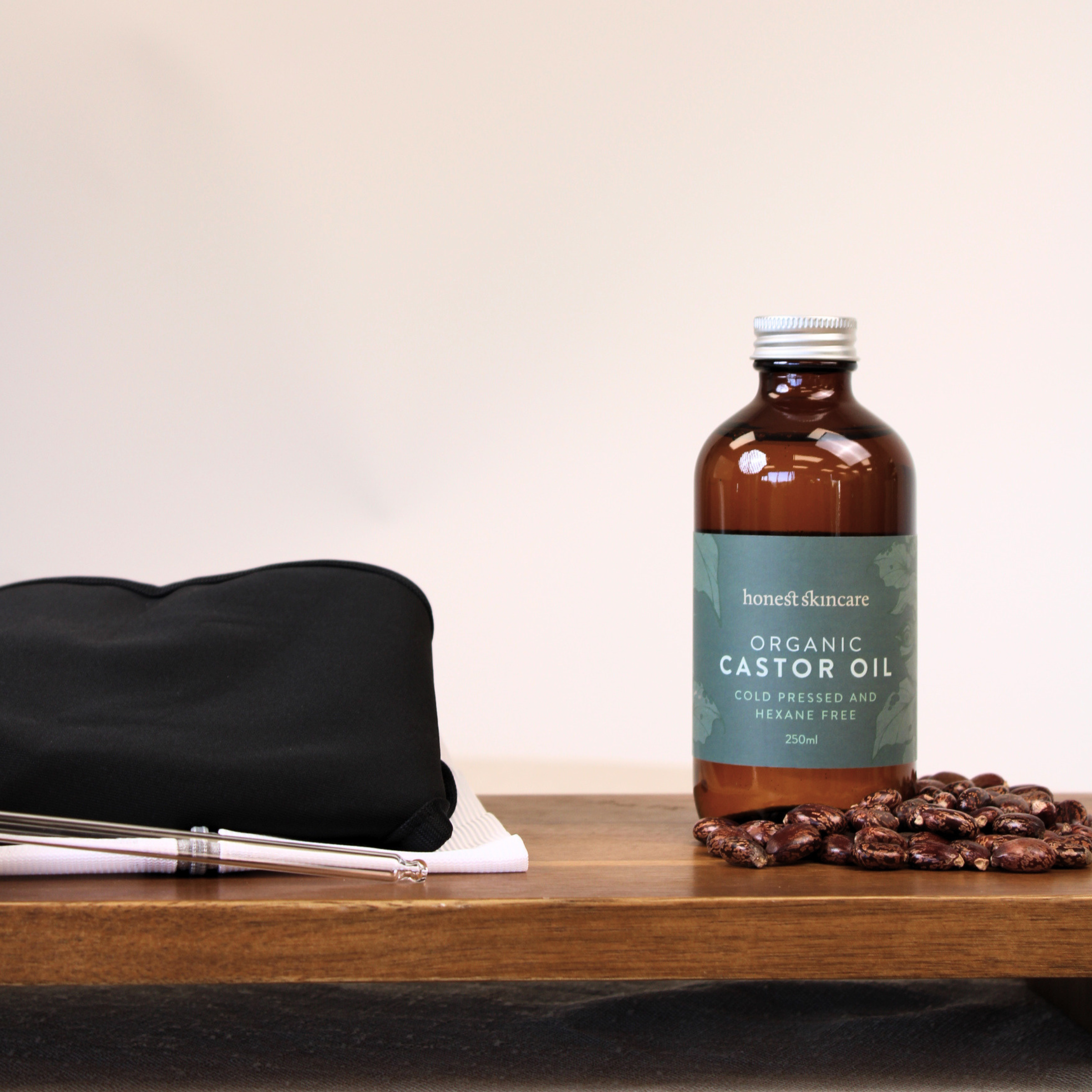 Bottle of organic castor oil on a wooden surface with castor beans and a black castor oil shoulder wrap