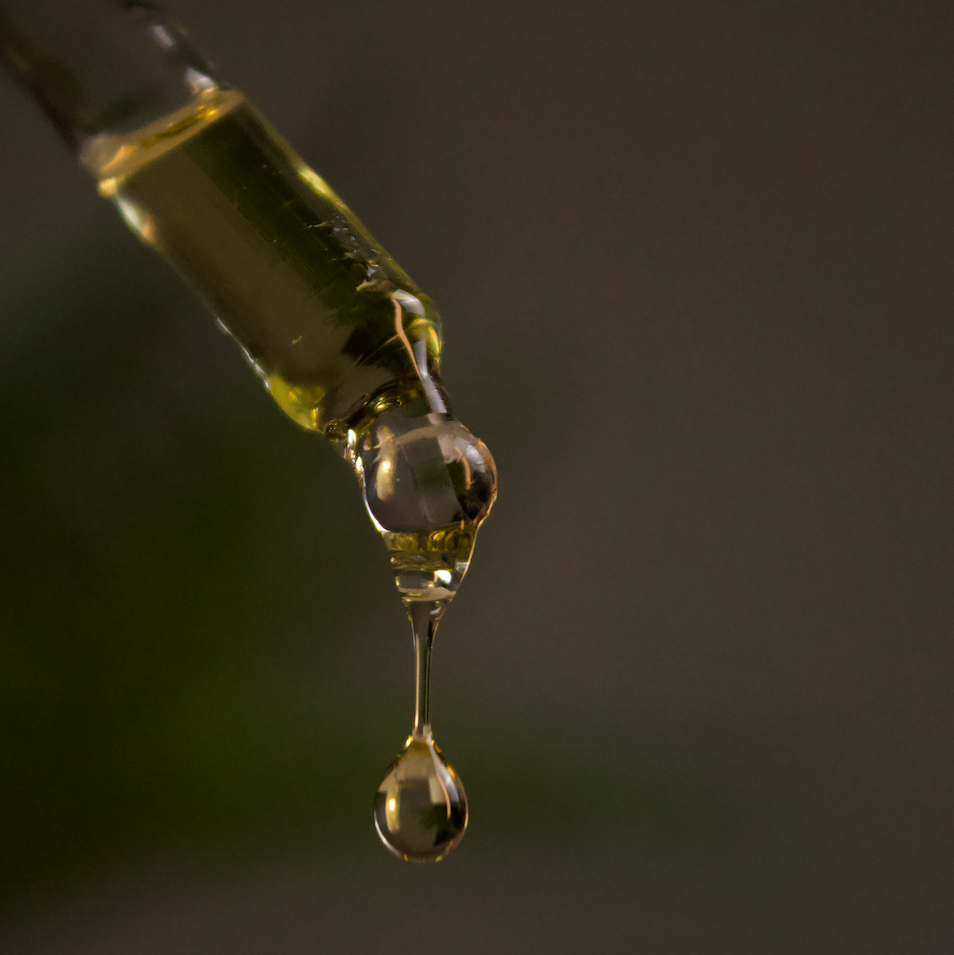 Close-up of a dropper with a drop of jojoba oil against a dark background