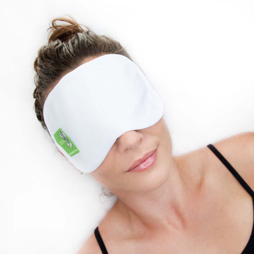 Woman wearing a white eye mask with castor oil pack for relaxation and wellness benefits.