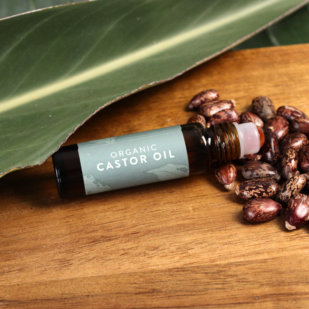 Roll-on bottle of organic castor oil on a wooden surface with castor beans and leaves.
