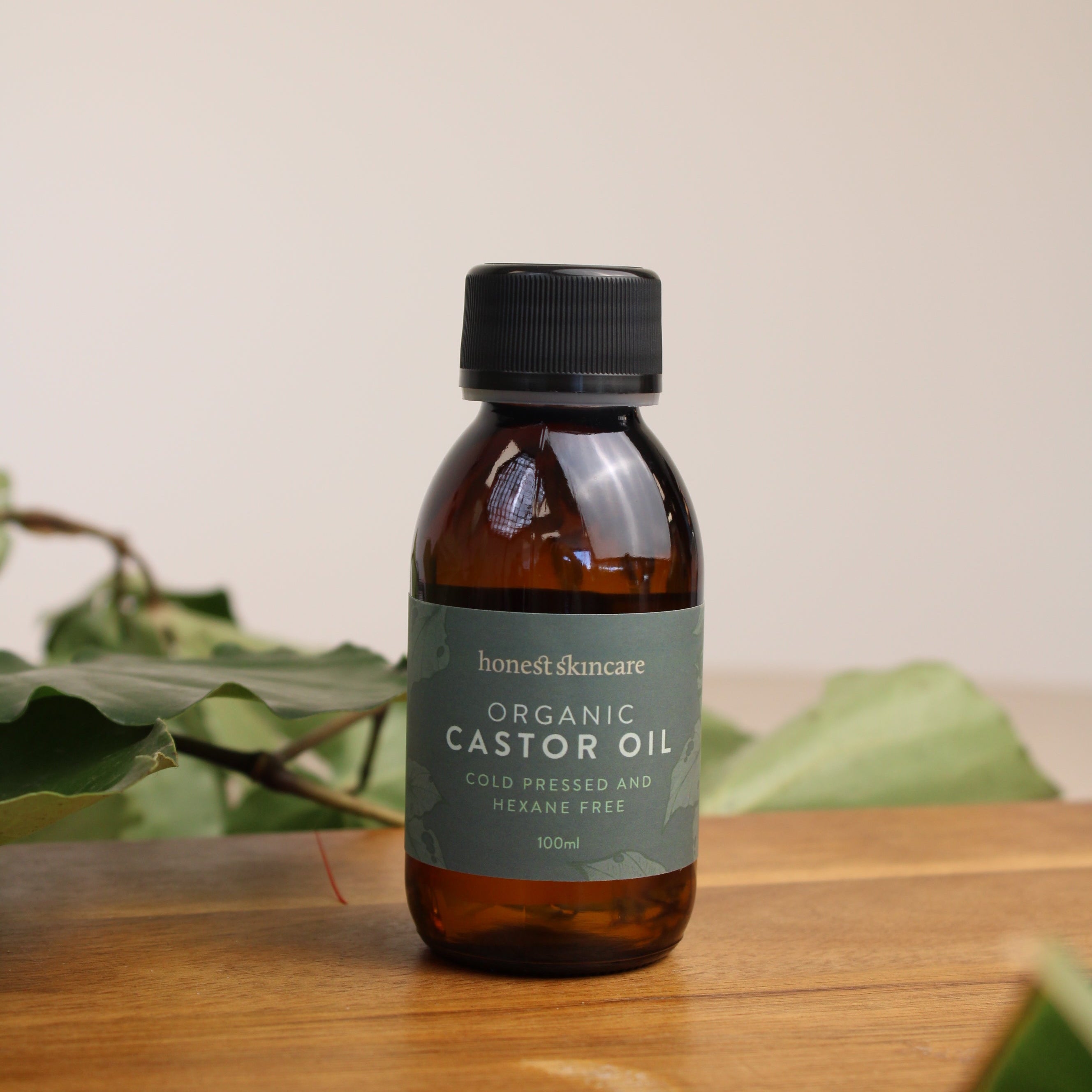 Bottle of castor oil 100ml on a wooden surface with a plant in the background
