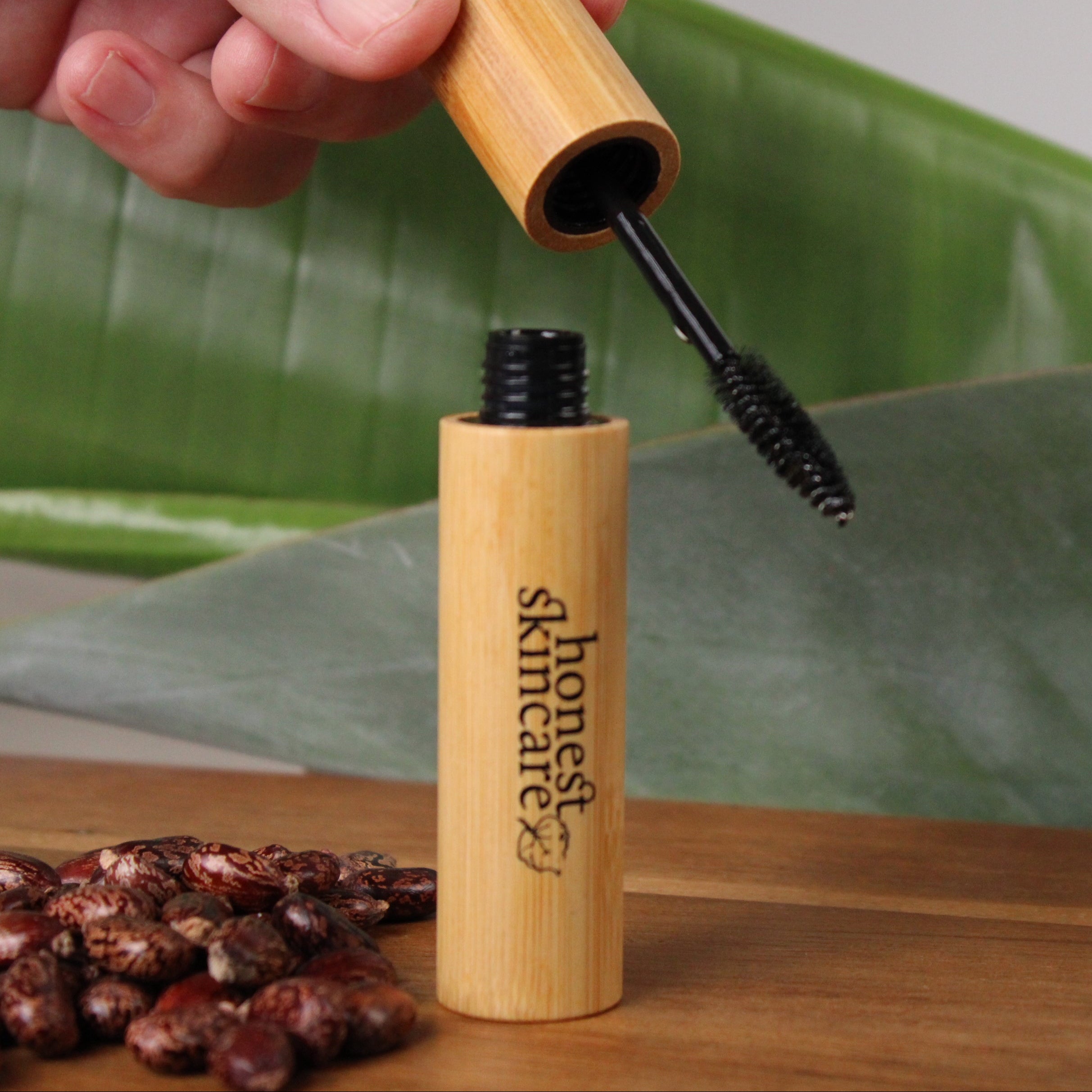 Bamboo castor oil masacara with ' honest skincare' branding on a wooden surface with green leaves in the background