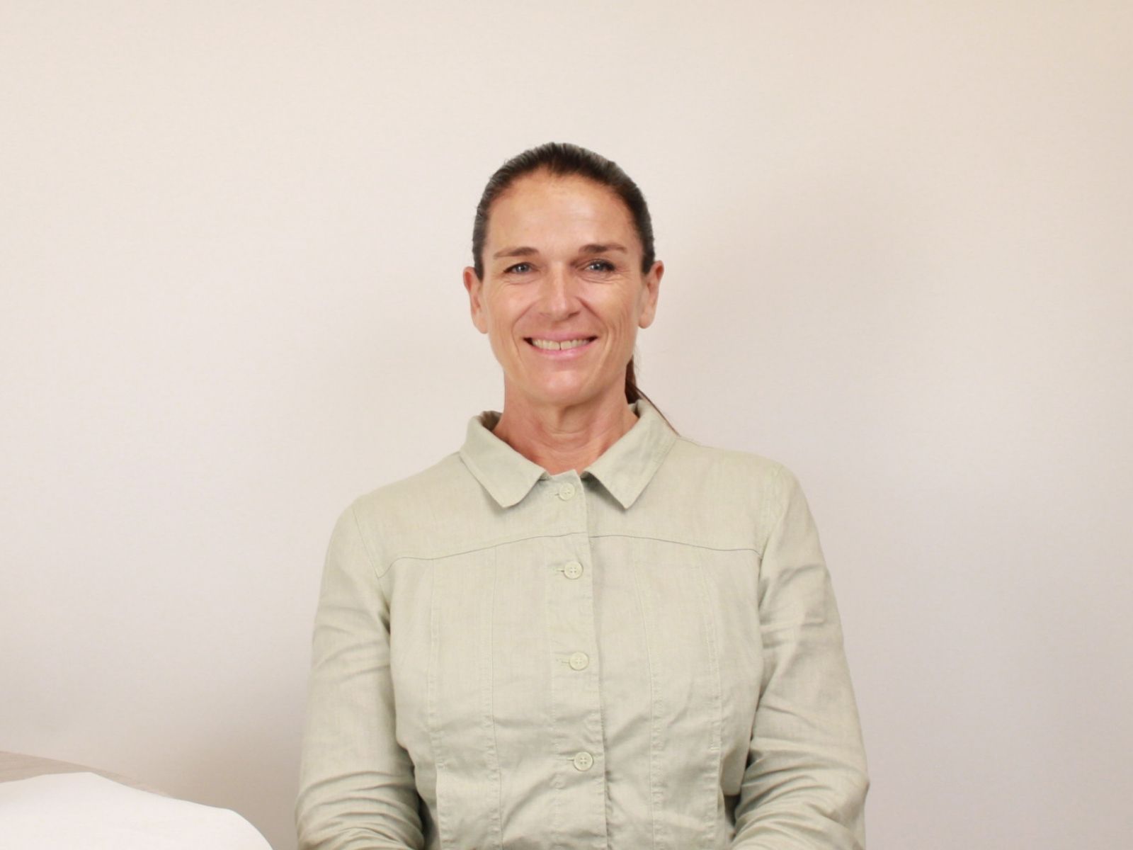 Smiling woman in a light green shirt, showcasing New Zealand facial mask technology and skincare.