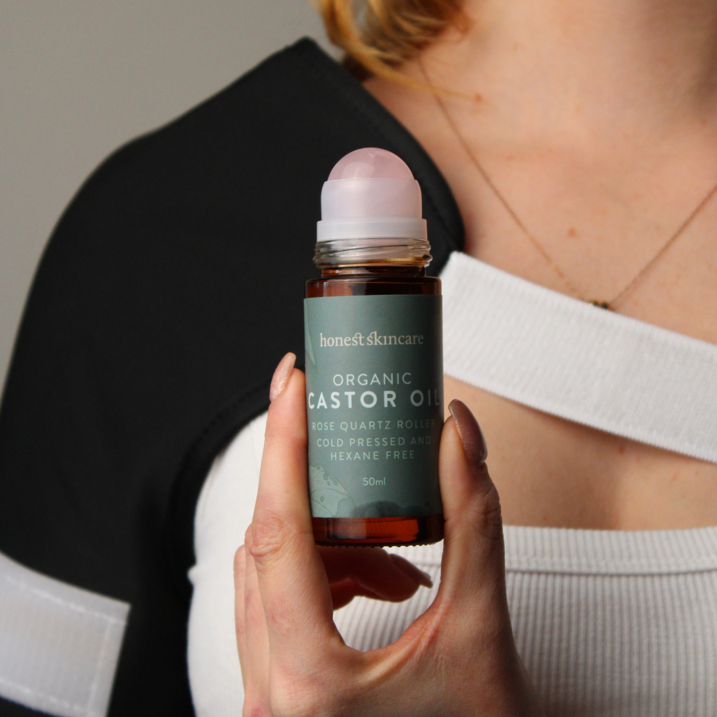 Person holding a bottle of 'honest skincare' organic castor oil quartz roller