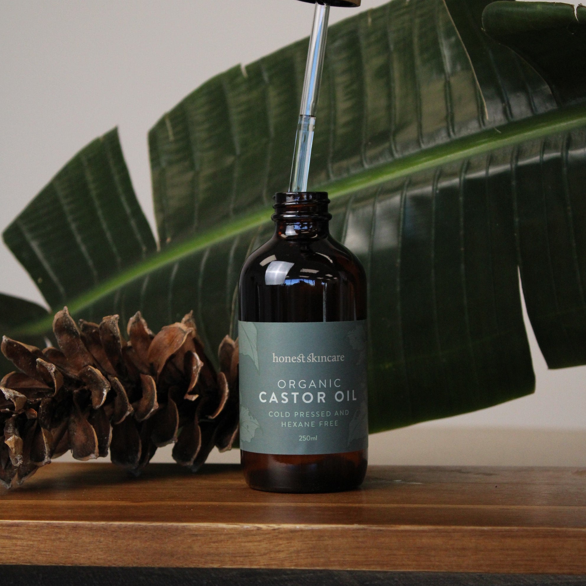 Bottle of castor oil being poured with a green leaf and pine cone in the background