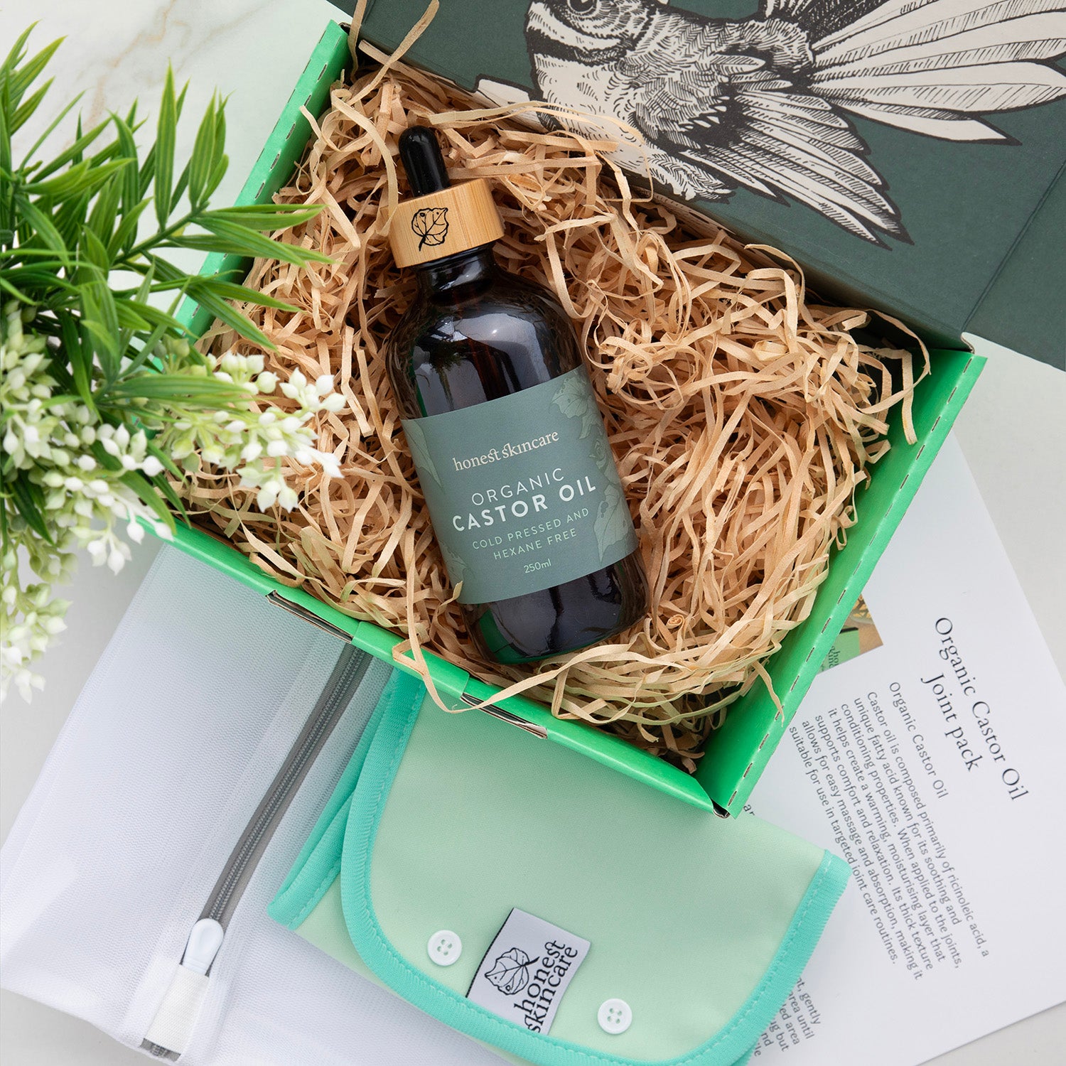 Honest skincares Bottle of organic castor oil in a decorative box with a  castor oil joint wrap plant and instructions on a white surface