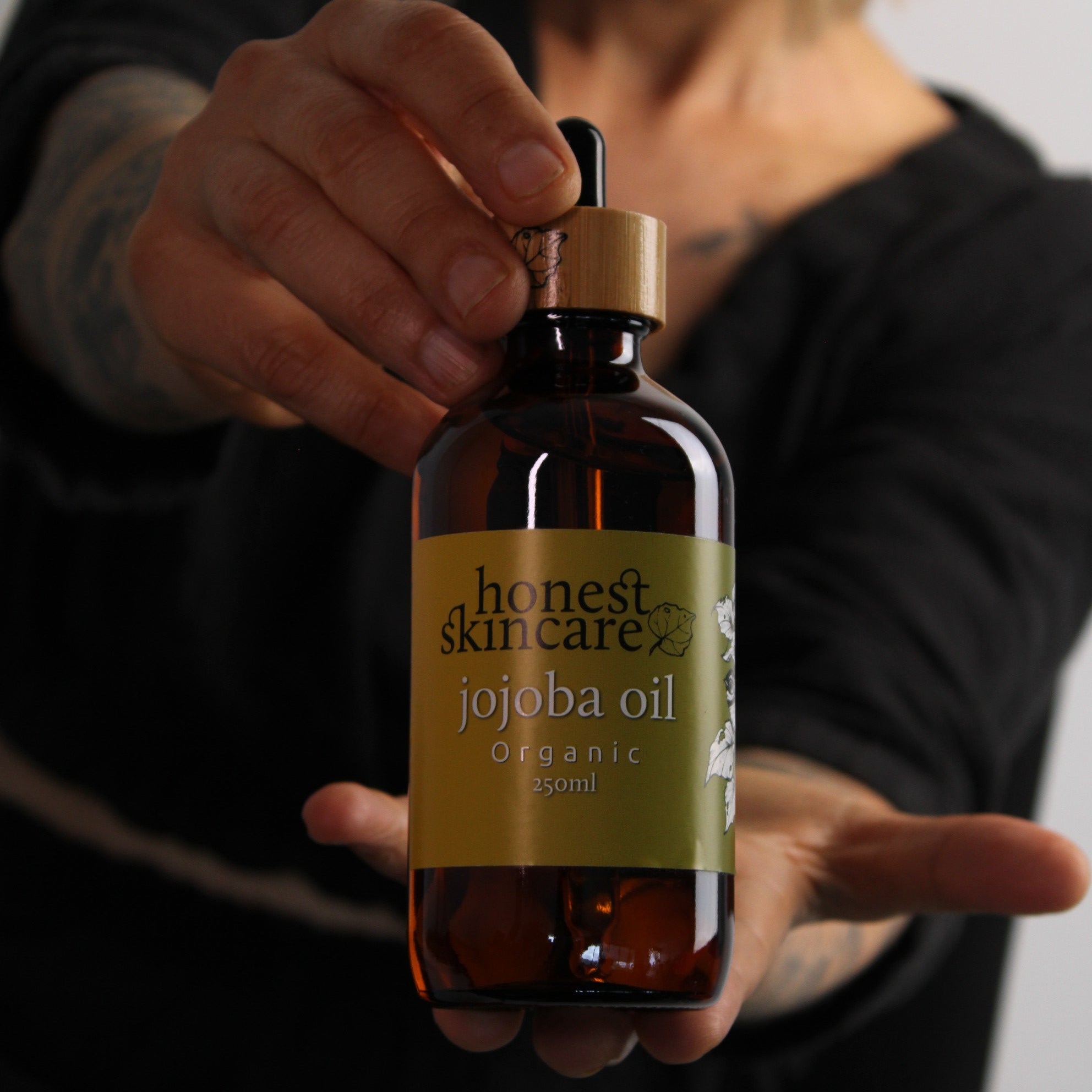 Hand holding a bottle of honest skincare jojoba with a label, against a blurred background