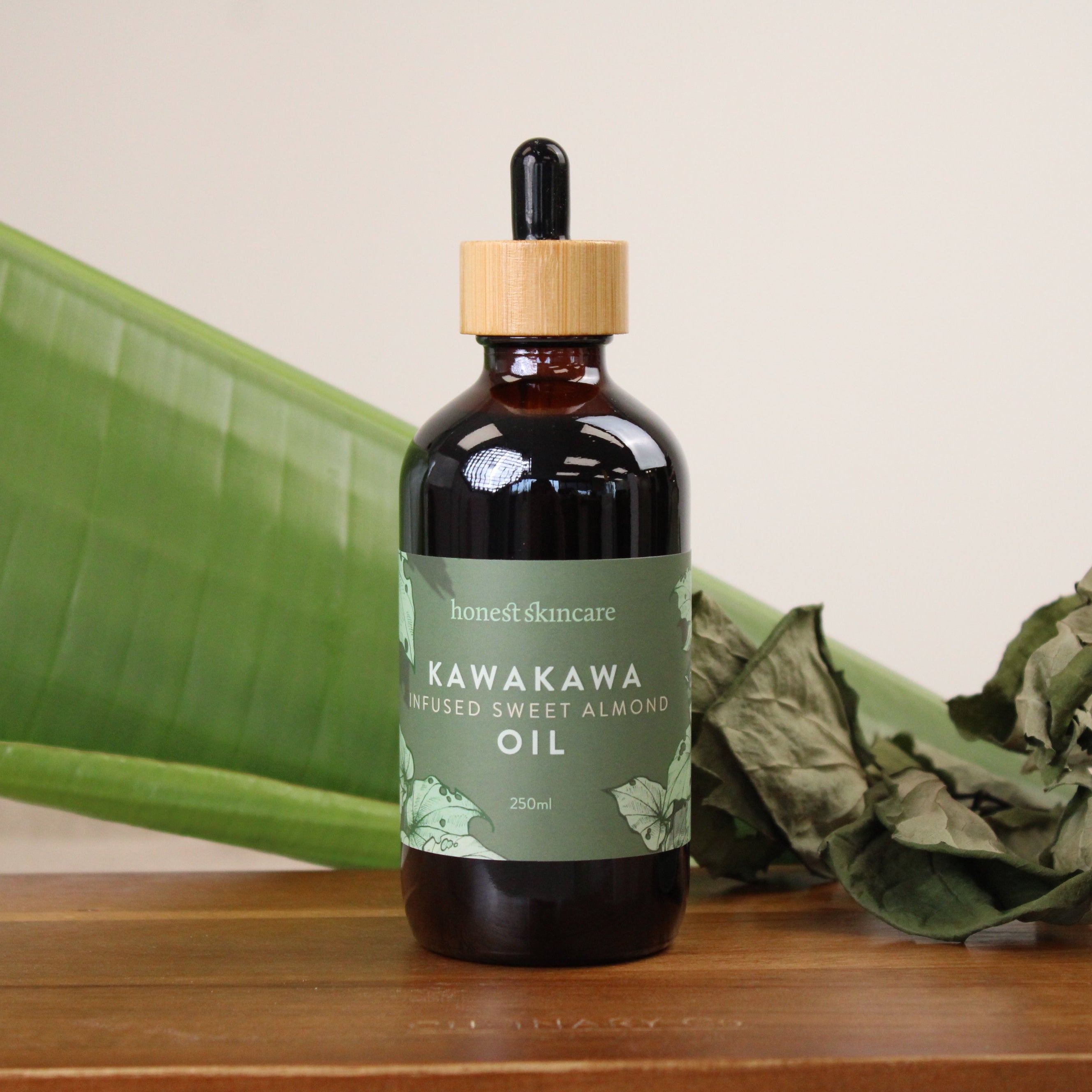 Bottle of Kawakawa infused with almond oil with green leaves on a wooden surface