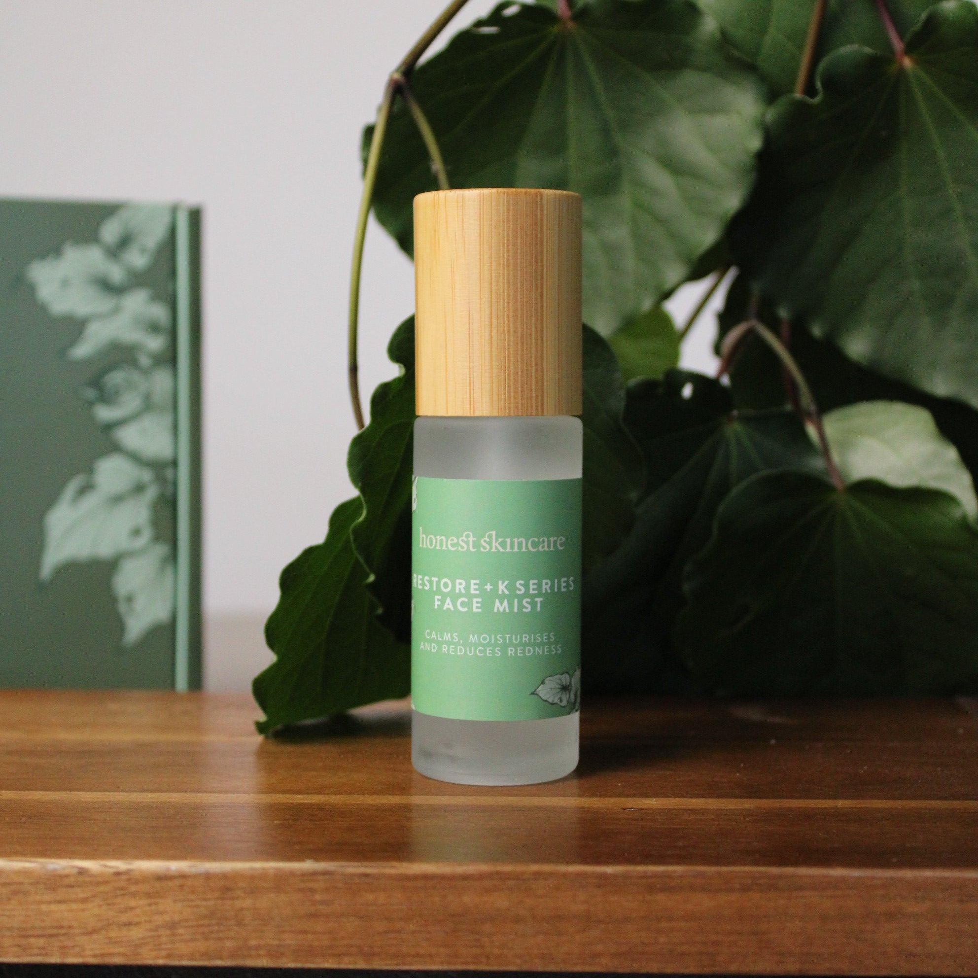 Bottle of skincare facial mist with green label on a wooden surface with leaves in the background Marine collagen melting mask korean skincare