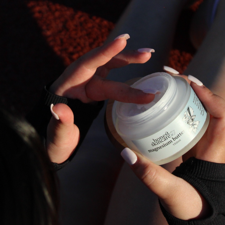 Person holding a jar of honest skincare magnesium butter with a blurred background