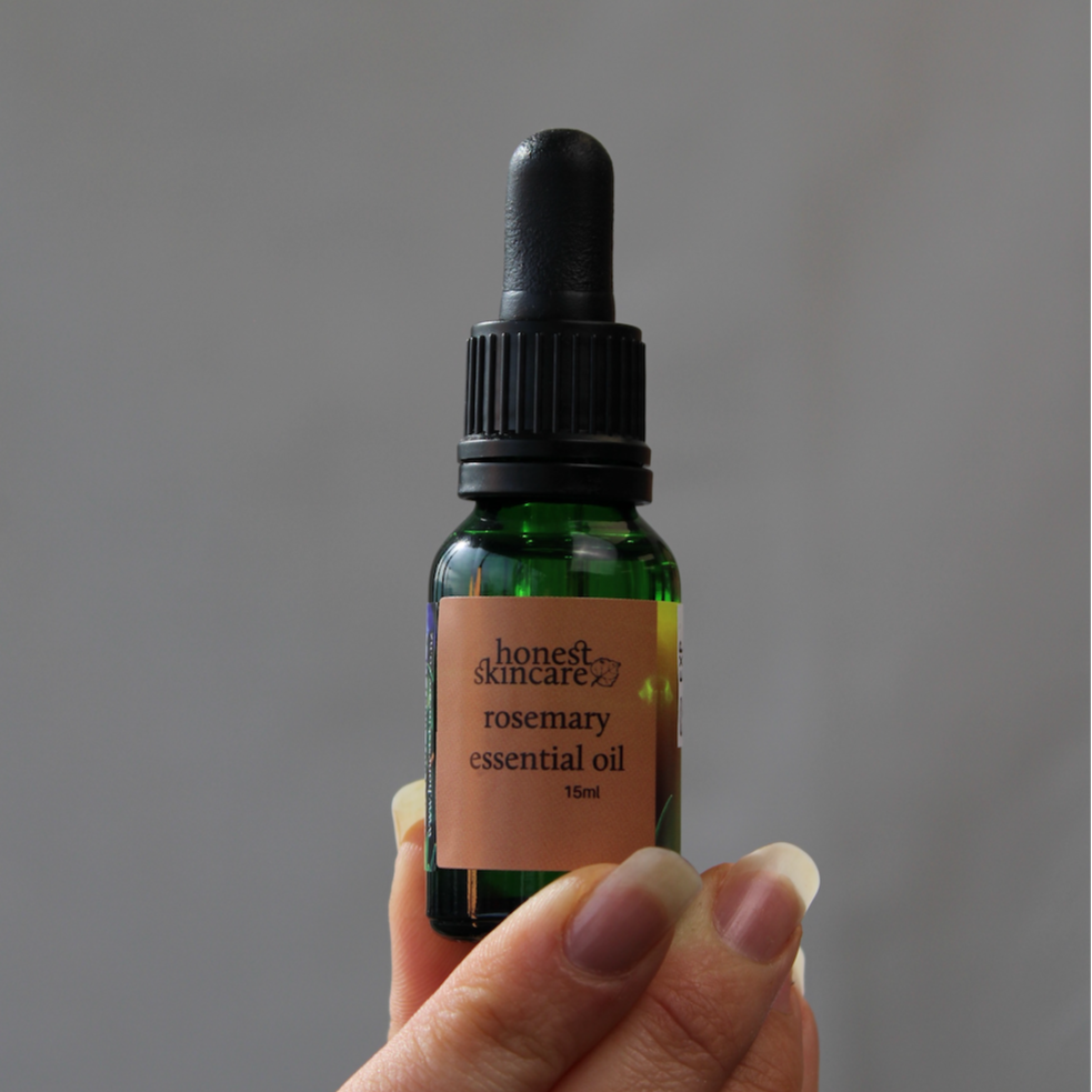Hand holding a bottle of honest skincare rosemary essential oil against a gray background