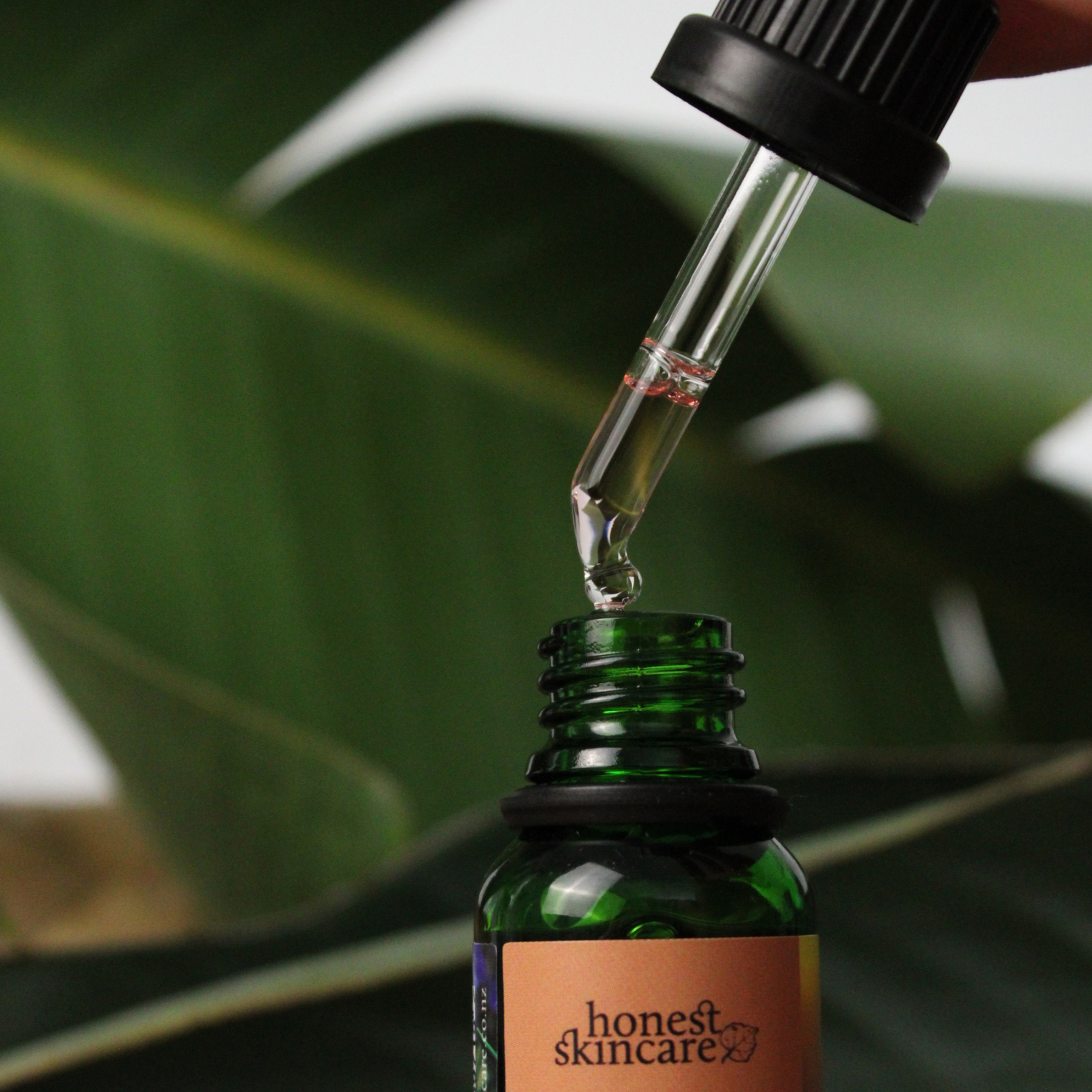 Green bottle with dropper labeled Rosemary essential oil 15ml honest skincare against a blurred green leaf background