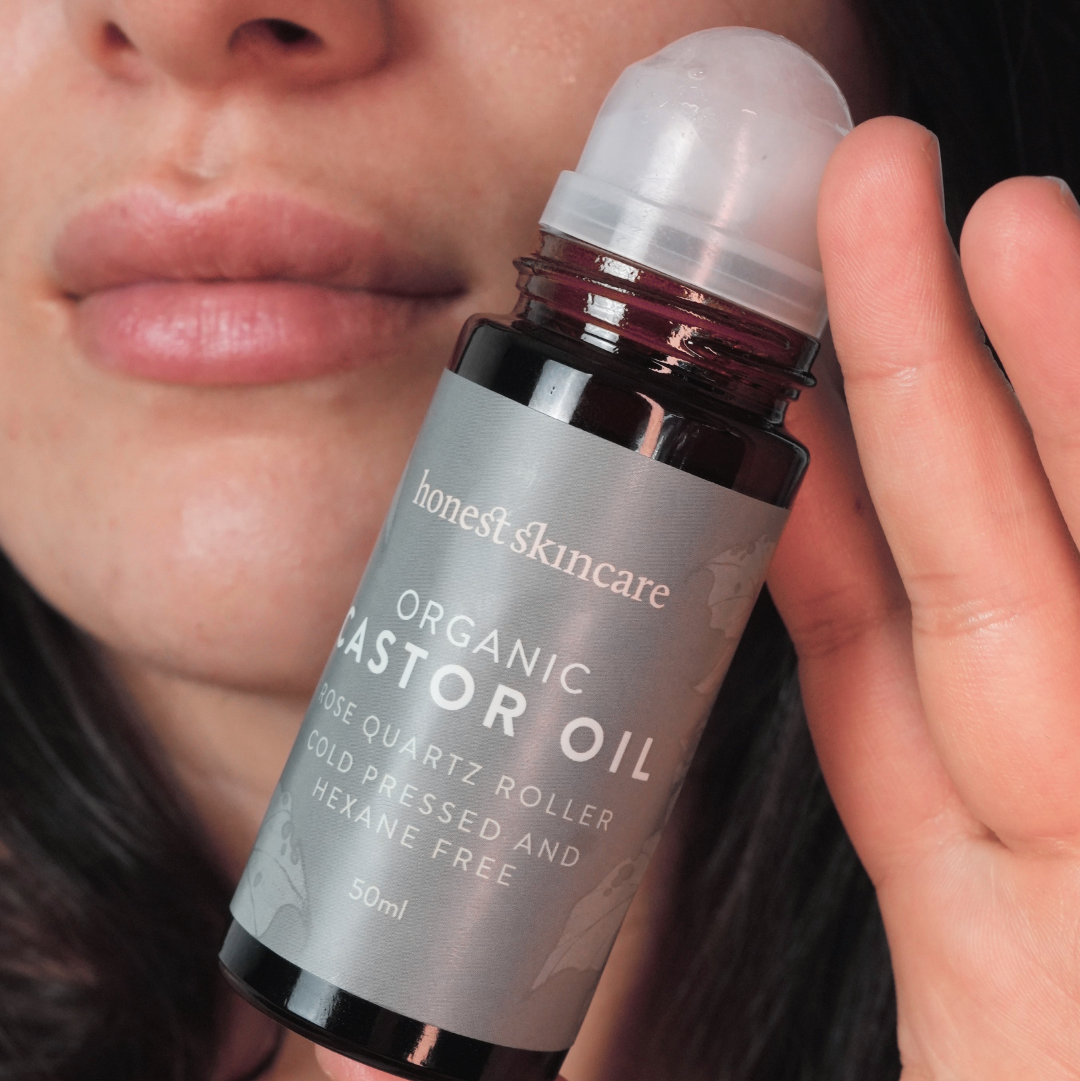 Hand holding a bottle of 'honest skincare' castor oil with a person's face in the background.