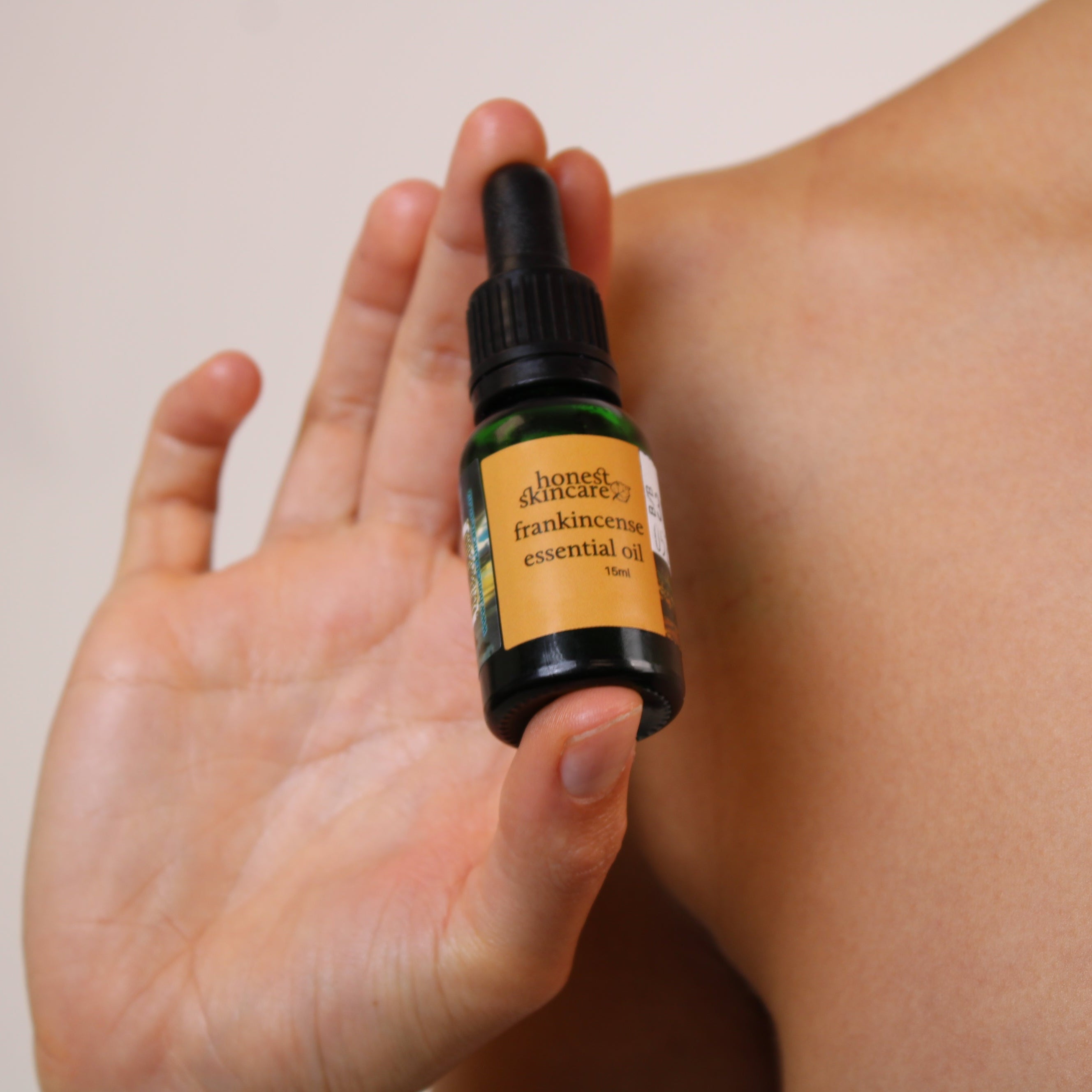 Hand holding a bottle of frankincense essential oil against a neutral background