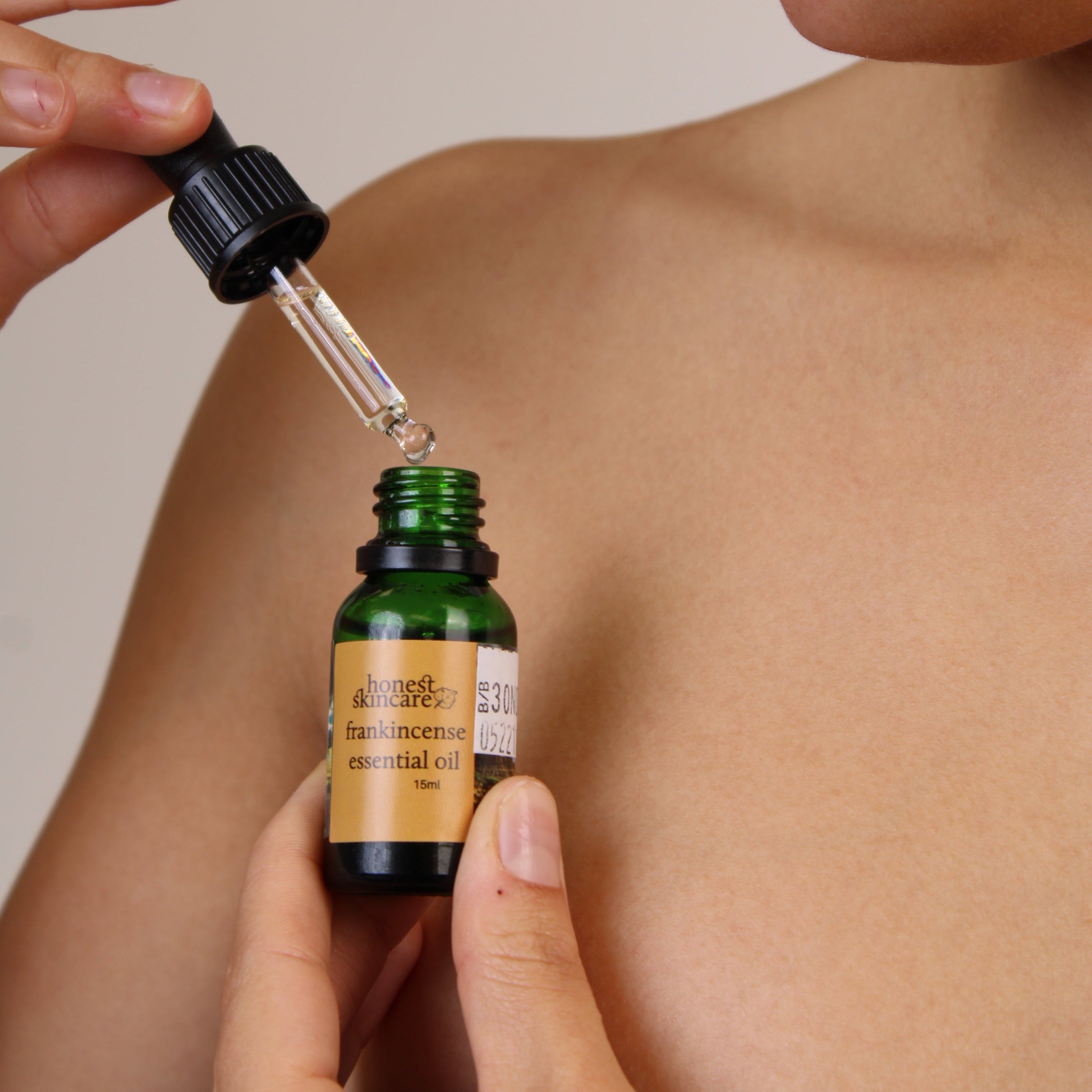Person applying a dropper of frankincense essential oil model  to their shoulder against a neutral background