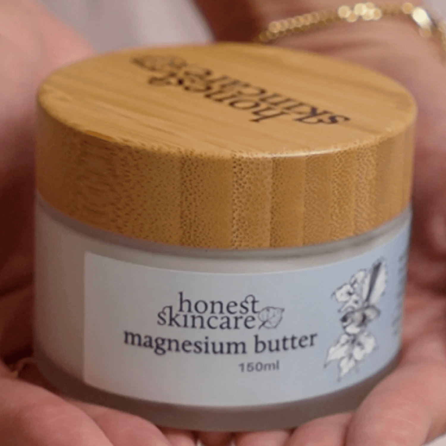 Jar of honest skincare magnesium butter held in hands with a wooden lid.