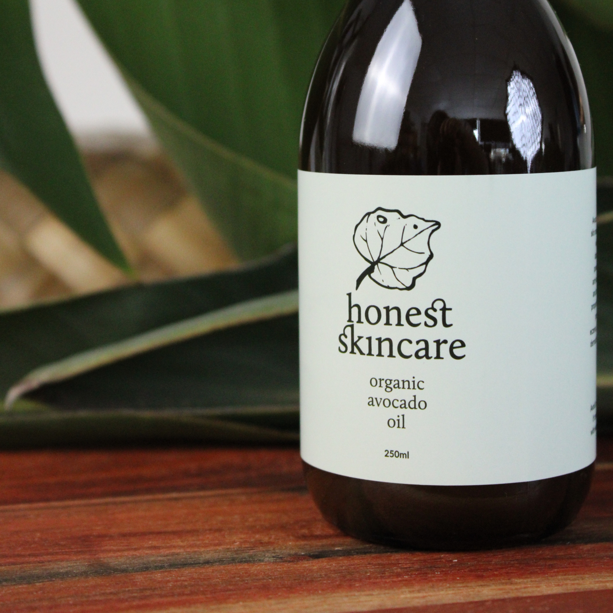 Bottle of honest skincare organic avocado oil on a wooden surface with a blurred green leaf background.