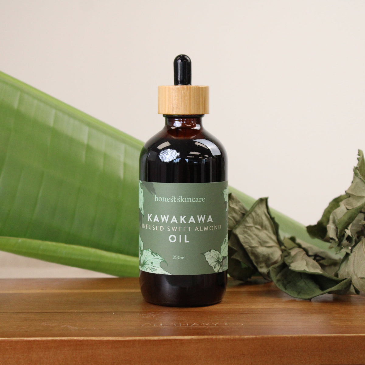 Bottle of Kawakawa oil with a dropper on a wooden surface with green leaves in the background