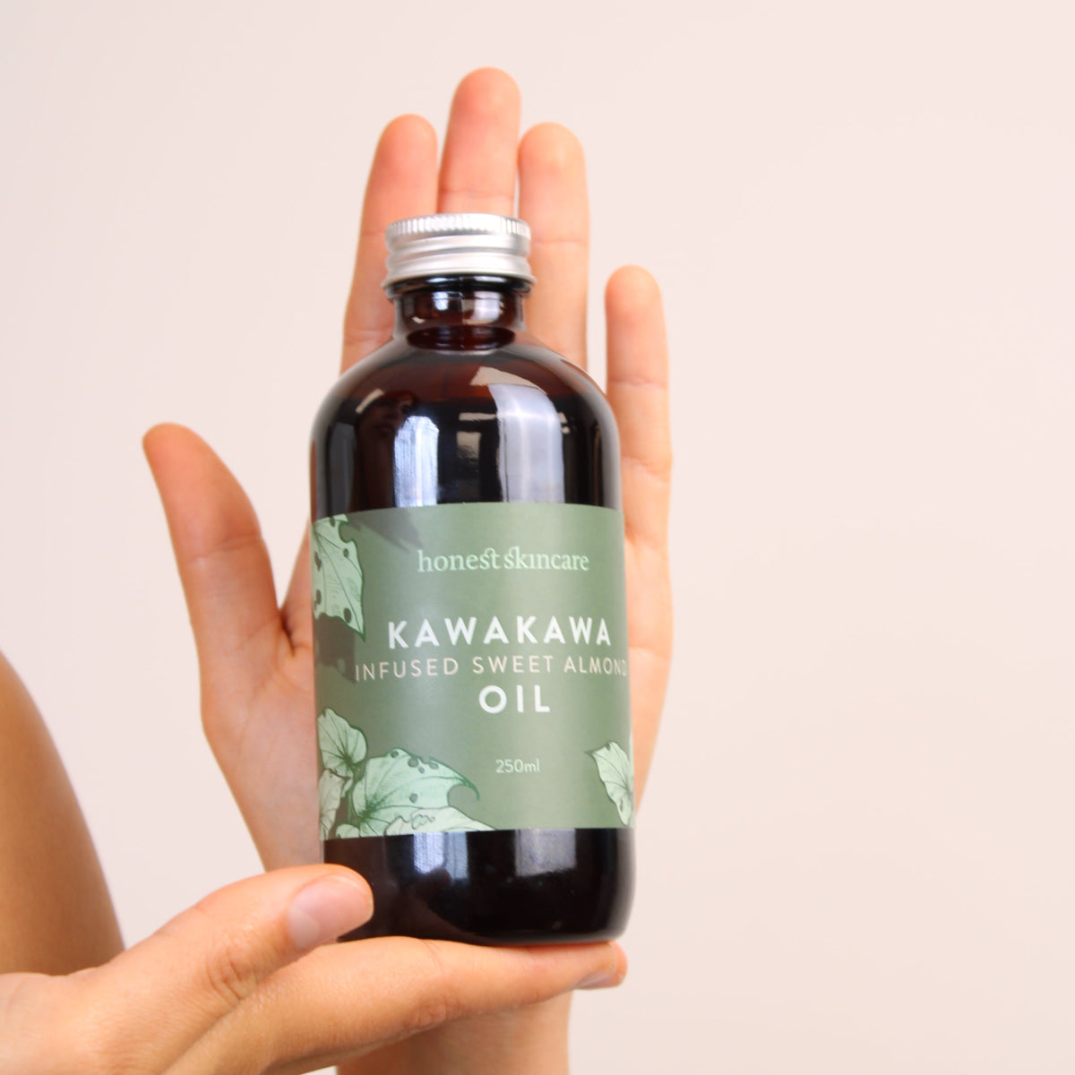 Hand holding a bottle of Kawakawa essential oil against a plain background