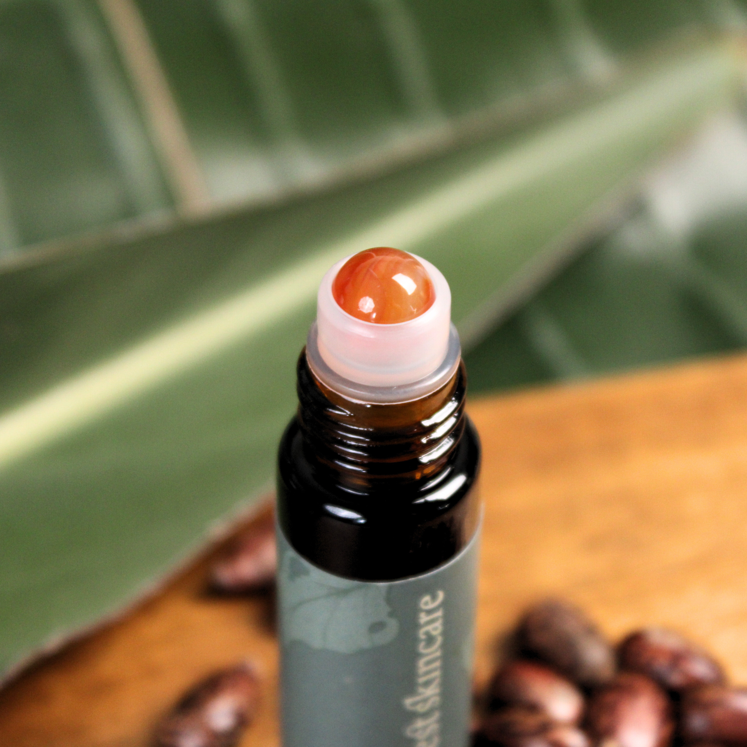 Roll-on bottle with a red roller ball on a wooden surface with leaves in the background