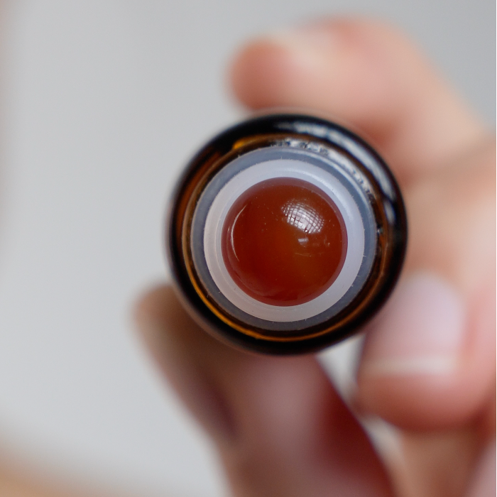 Hand holding a small brown bottle with a white cap, blurred background