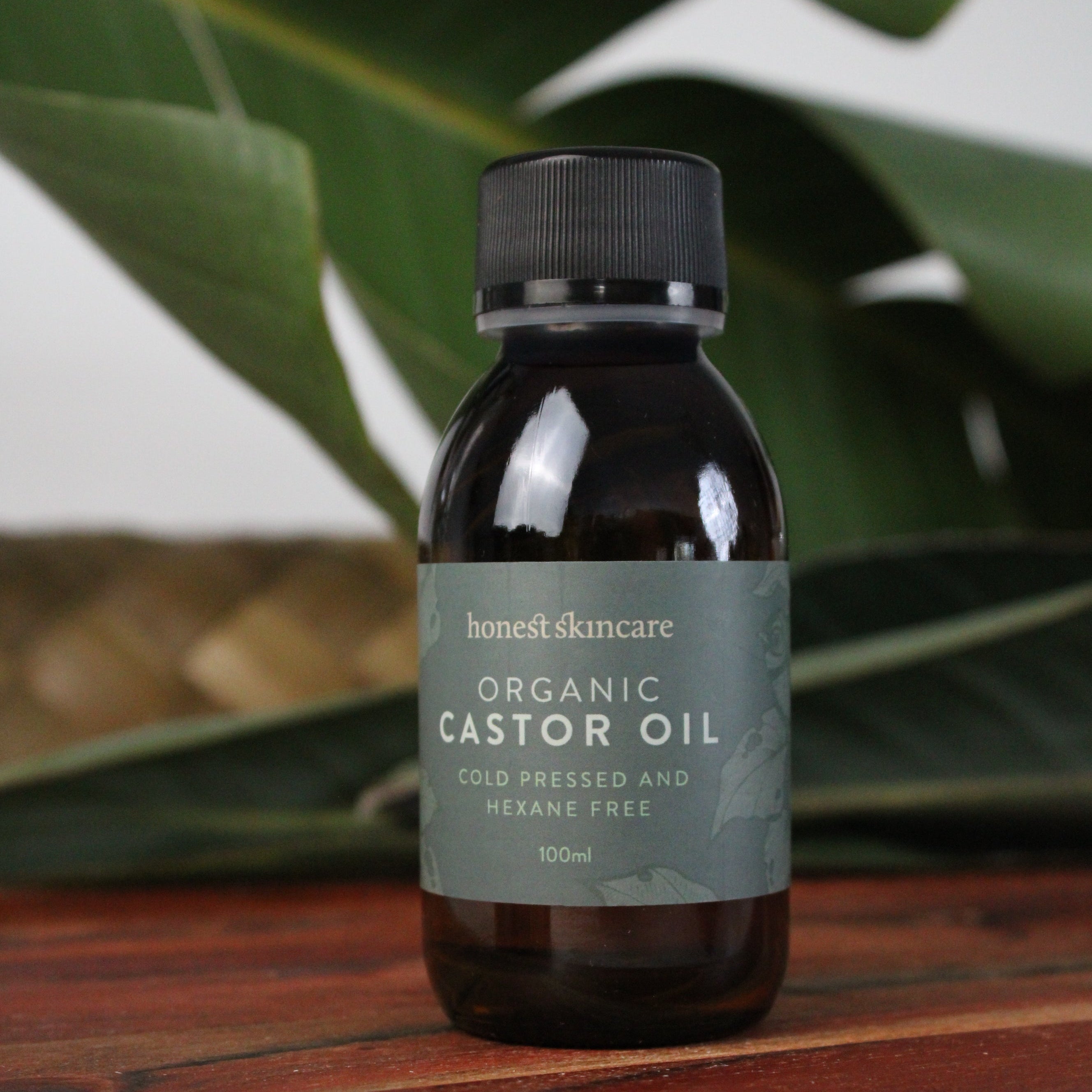 Bottle of organic castor oil with a label on a wooden surface and plant in the background
