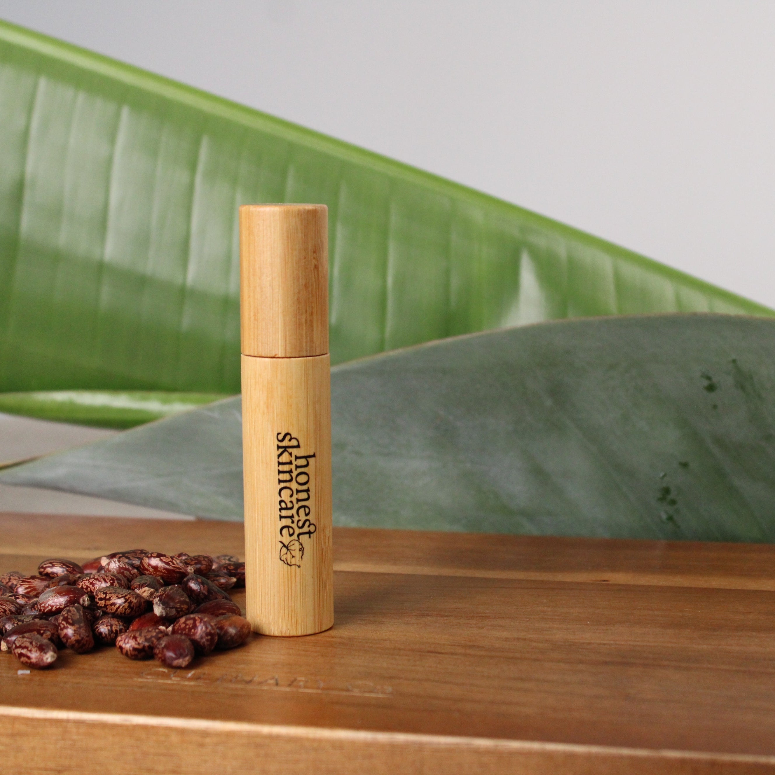 Bamboo castor oil mascara with ' honest skincare' branding on a wooden surface with green leaves in the background