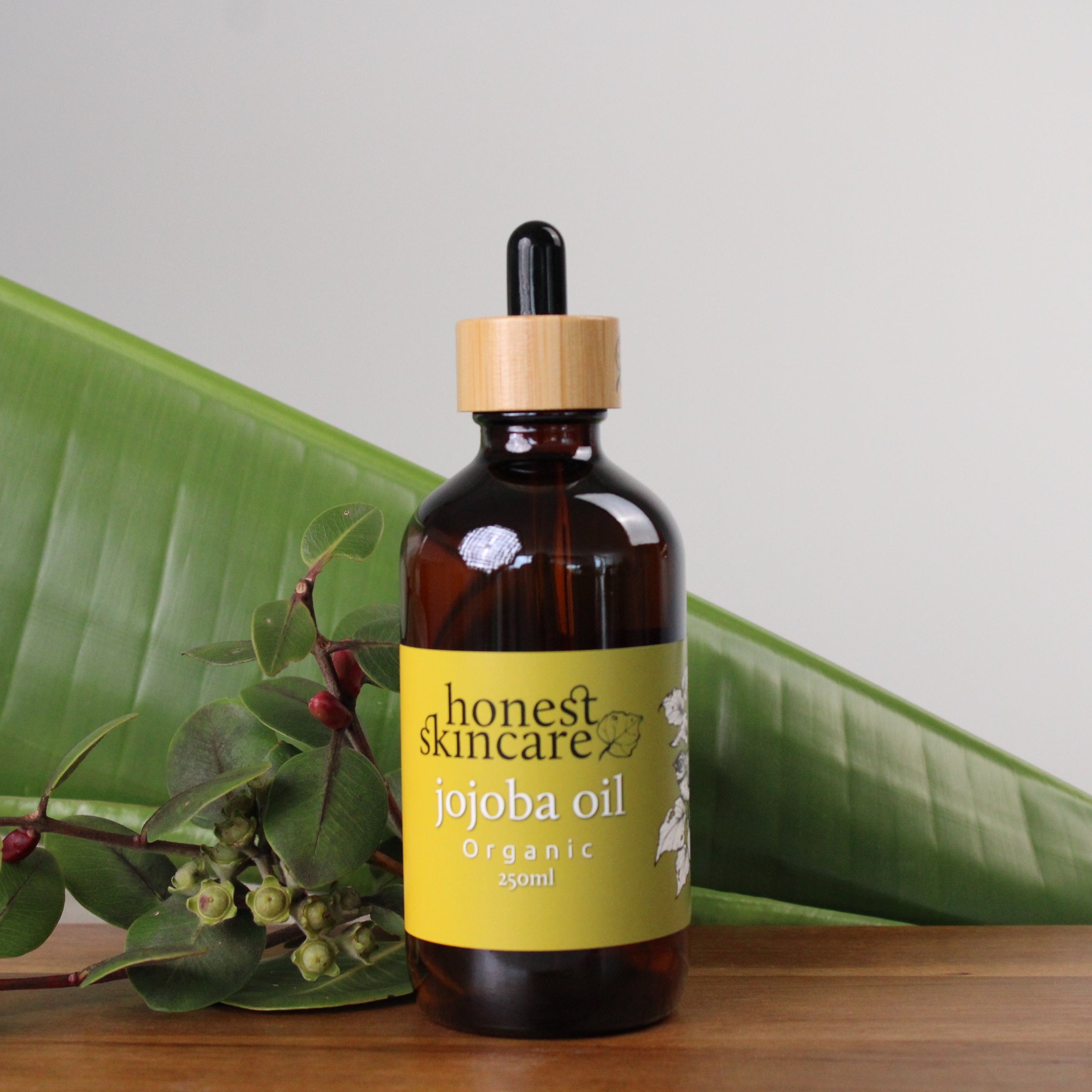 Bottle of  honest skincares organic jojoba oil with a dropper on a wooden surface with green leaves in the background