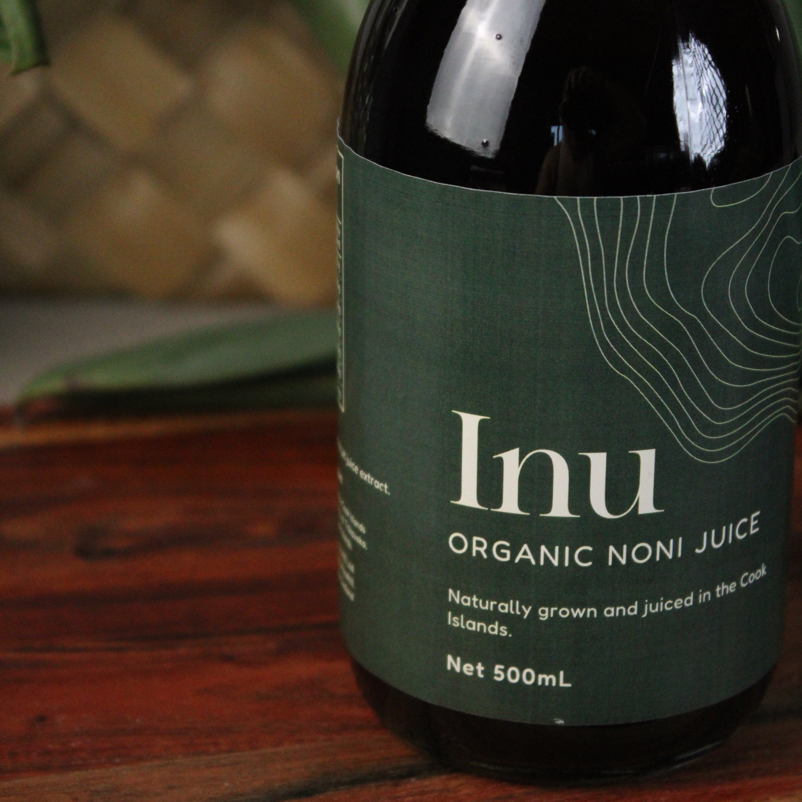 Bottle of Inu Organic Noni Juice with a green label on a wooden surface.