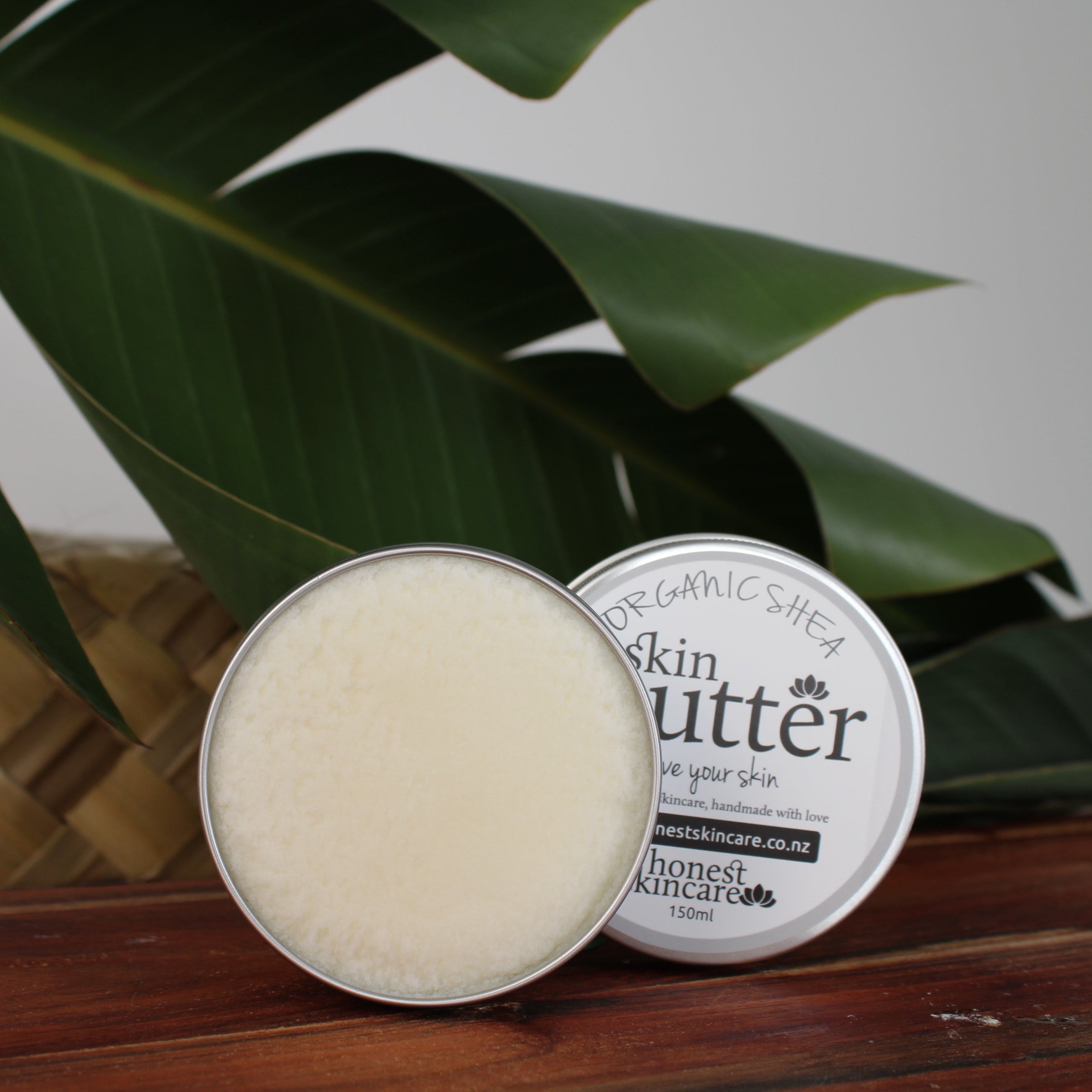 organic shea butter tin honest skincare  on a wooden surface with green leaves in the background