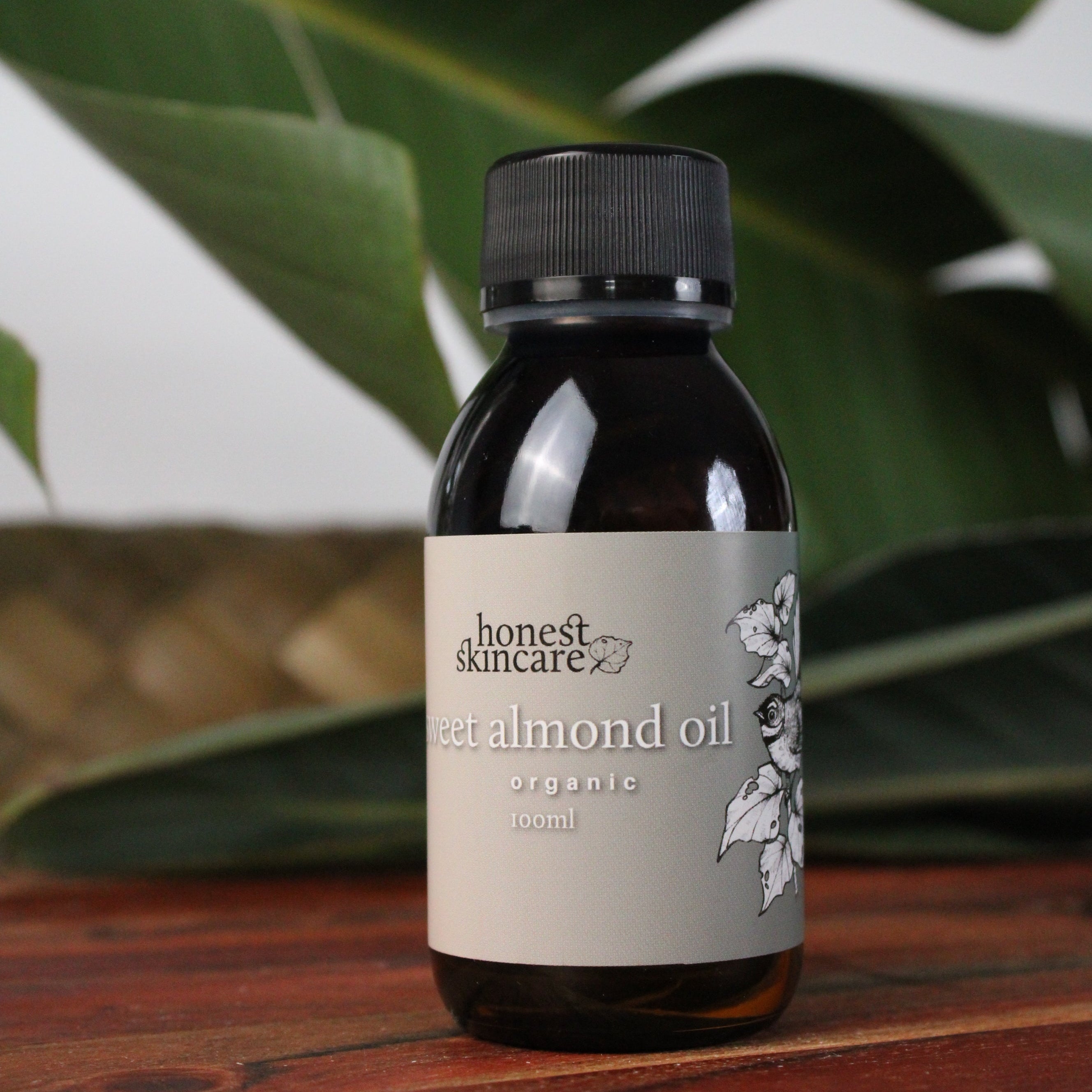 Bottle of organic almond oil with a label on a wooden surface and plant in the background
