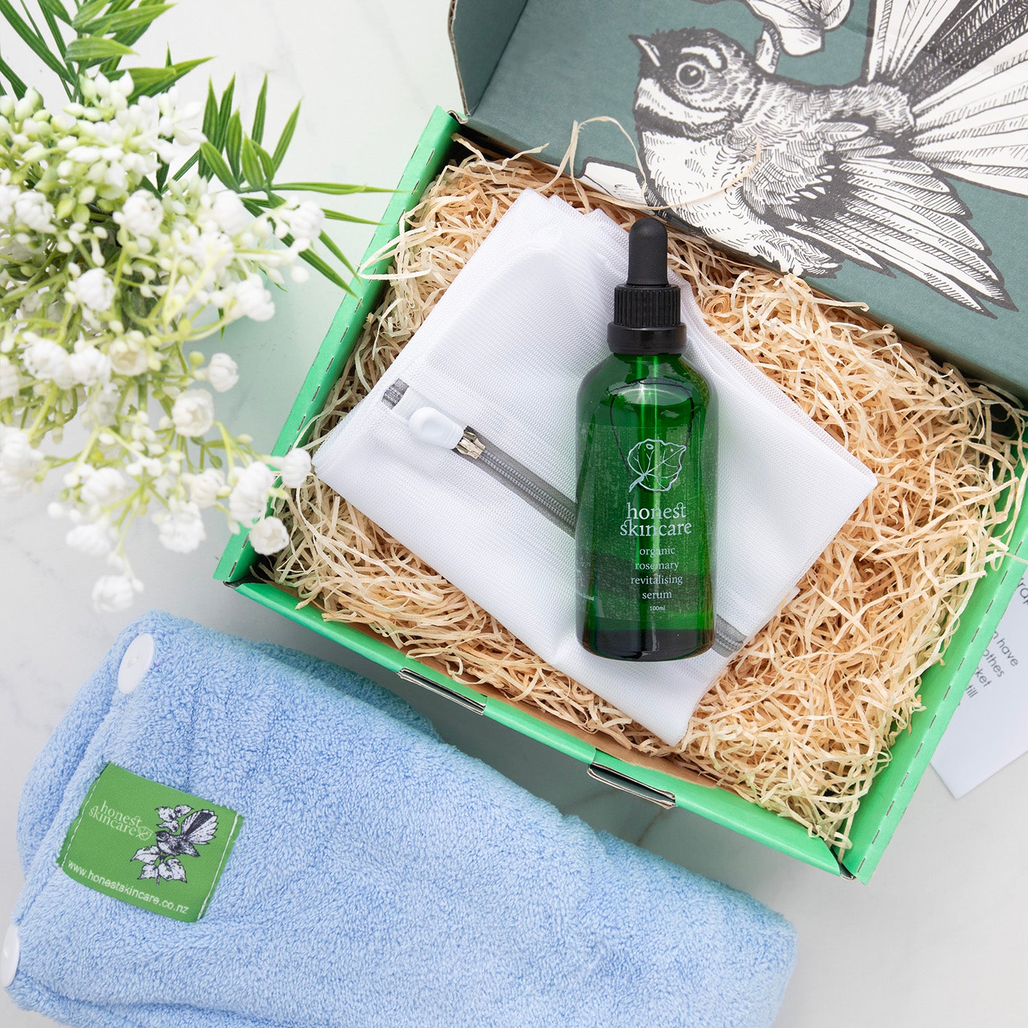rosemary hair serum skincare bottle with a towel and flowers on a white background