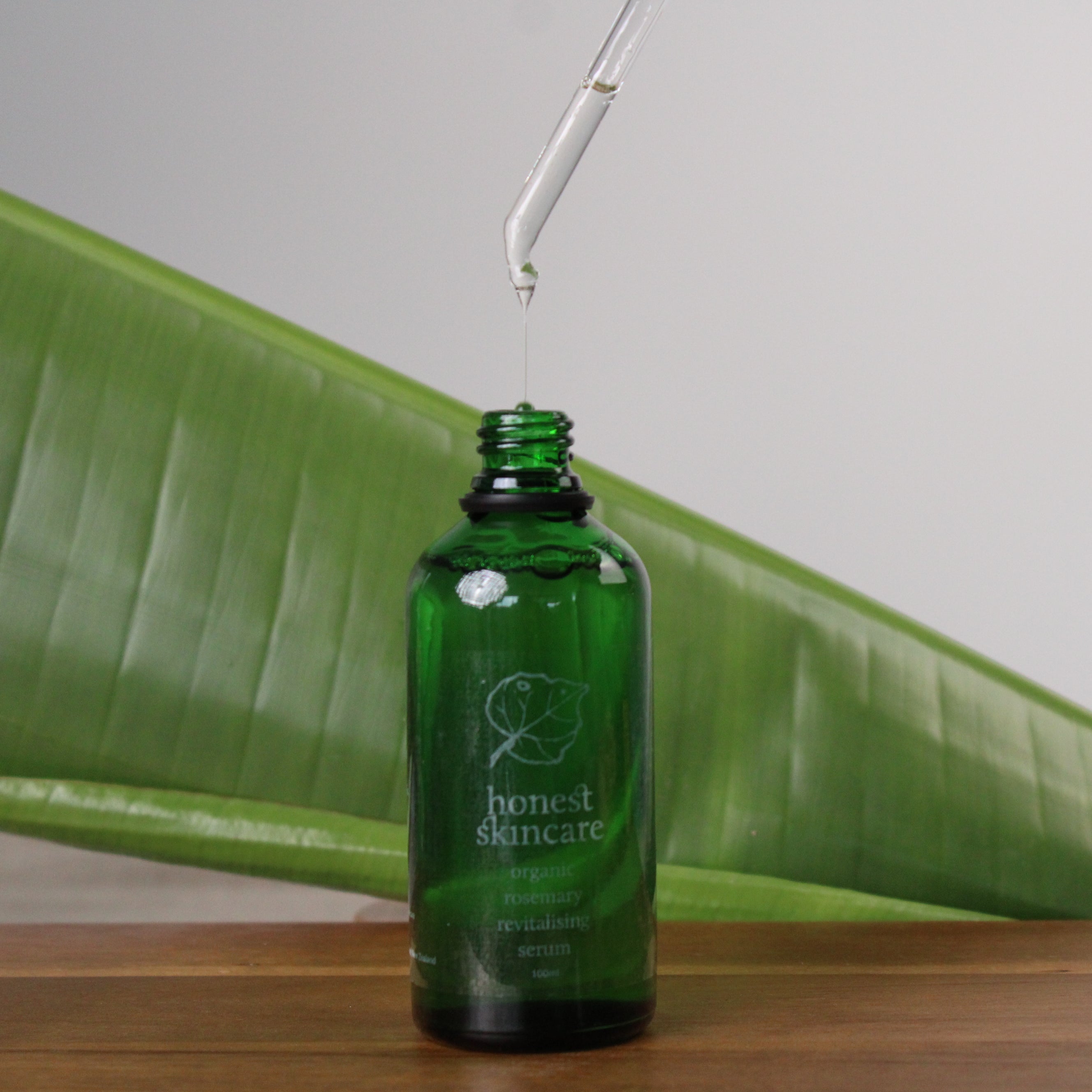Revitalising Rosemary 'honest skincare' with a dropper on a wooden surface with a leaf in the background.